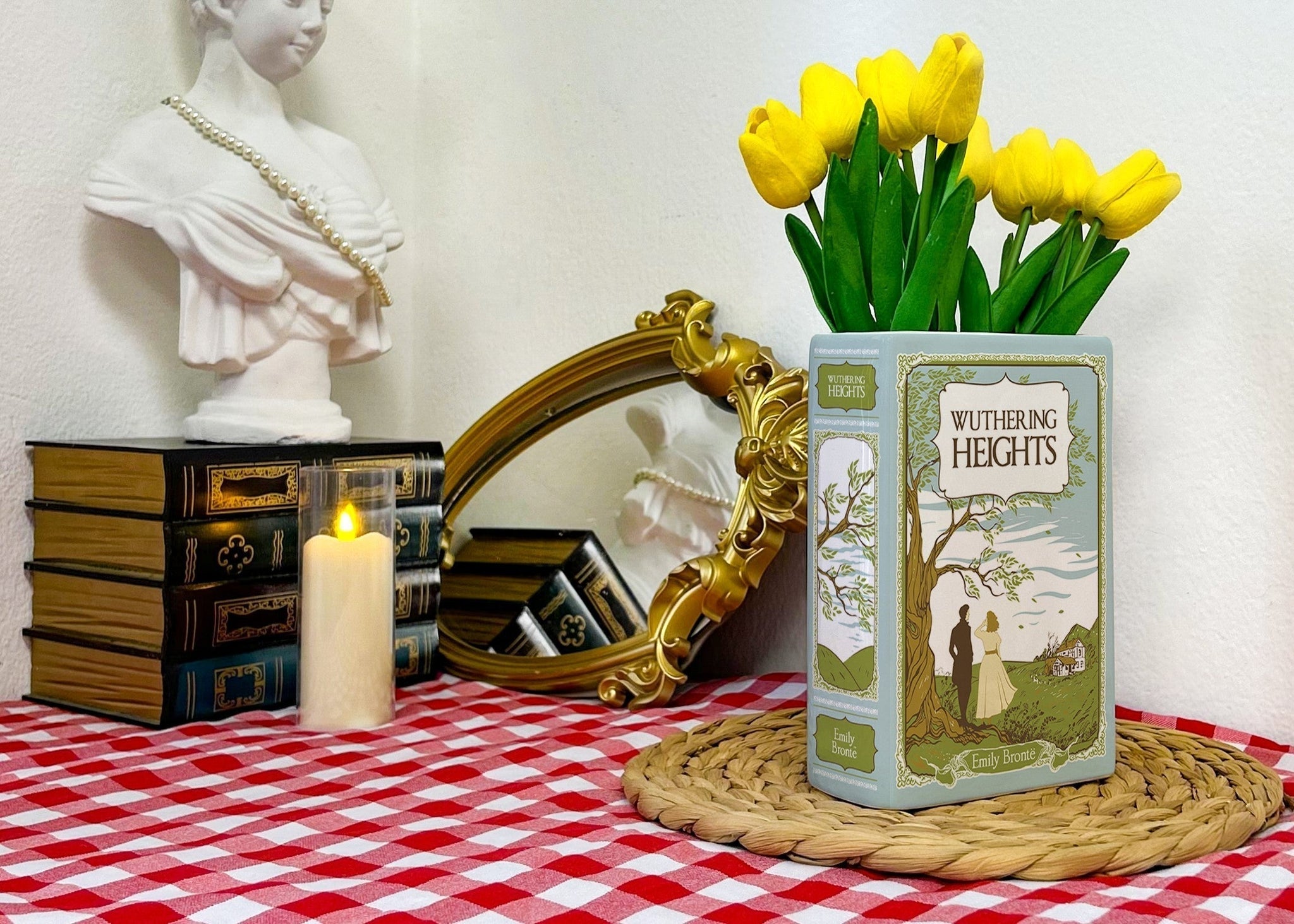 Wuthering Heights book with yellow tulips on a checkered table near a bust, candle, and mirror