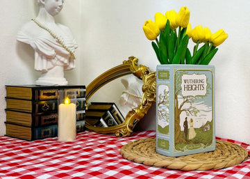 Wuthering Heights book with yellow tulips on a checkered table near a bust, candle, and mirror