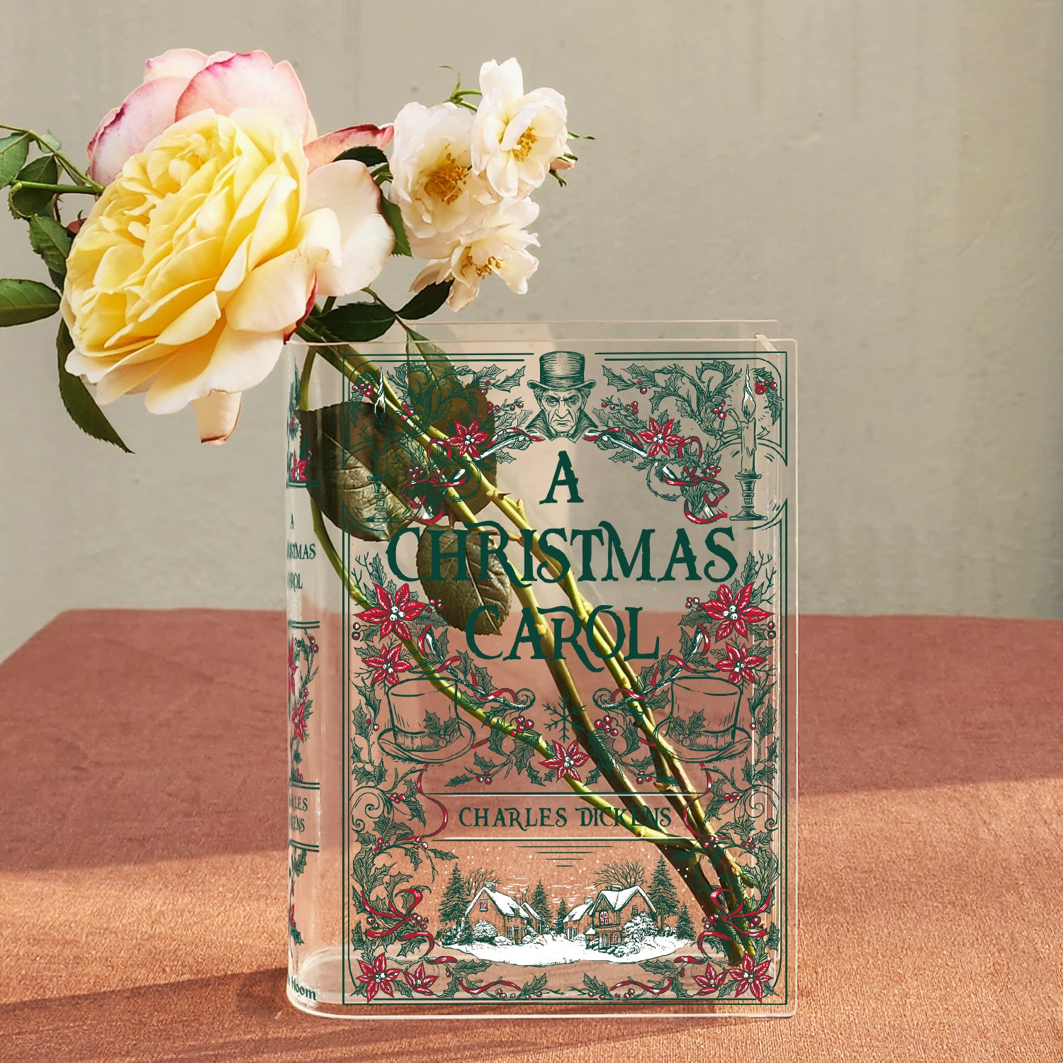 A Christmas Carol acrylic book vase with fresh roses on a pink surface