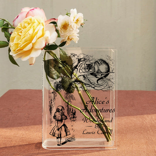 Alice's Adventures in Wonderland acrylic book vase with yellow and white roses on a brown table