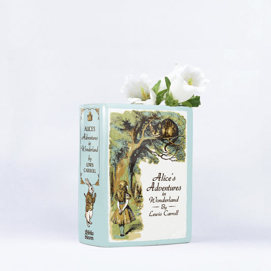 Alice's Adventures in Wonderland ceramic book vase with white flowers on white background
