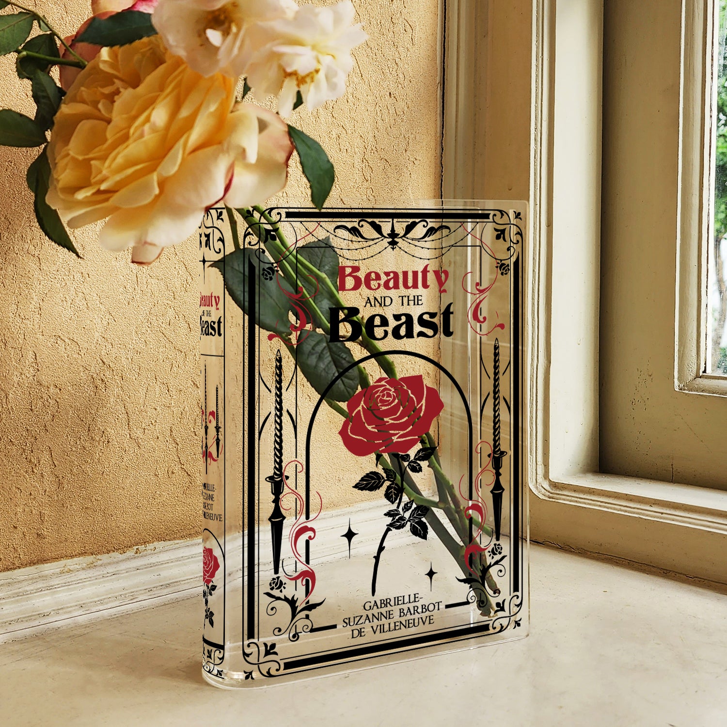 Beauty and the Beast acrylic book vase with yellow roses by a window on a beige surface
