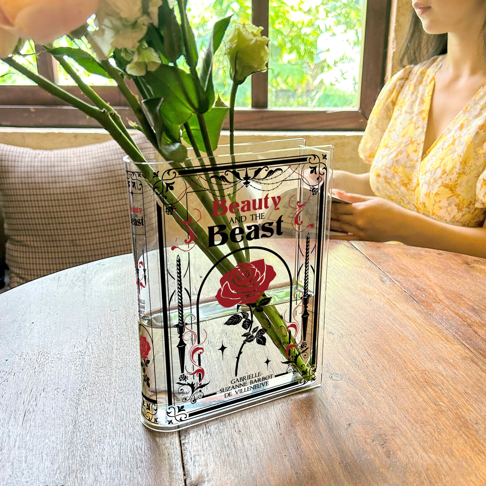 Beauty and the Beast acrylic book vase with flowers on wooden table in sunlit cafe