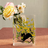 Acrylic book-shaped vase with yellow flowers and black cat illustration on table