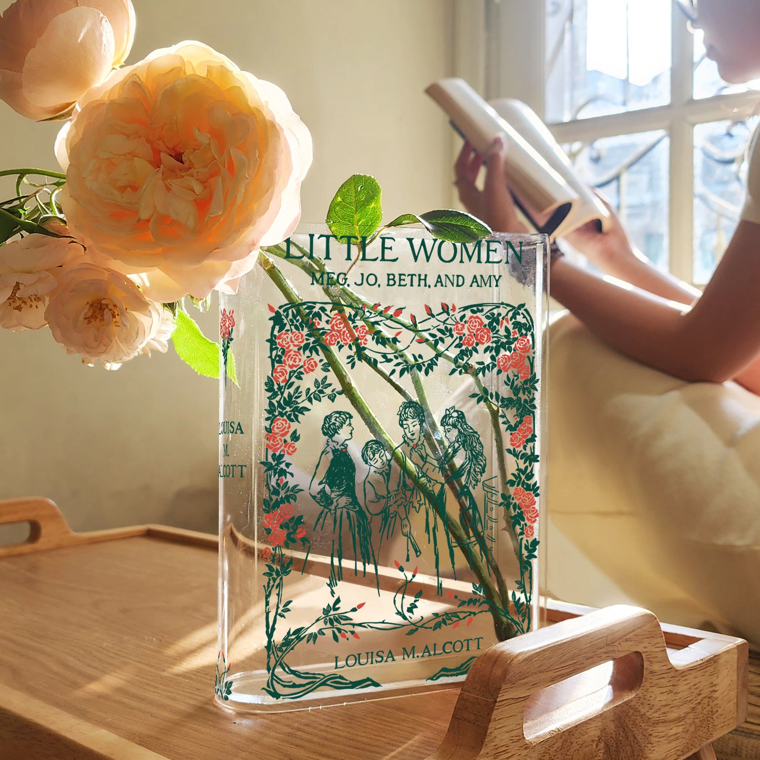 Little Women acrylic book vase with flowers on wooden tray, woman reading by window