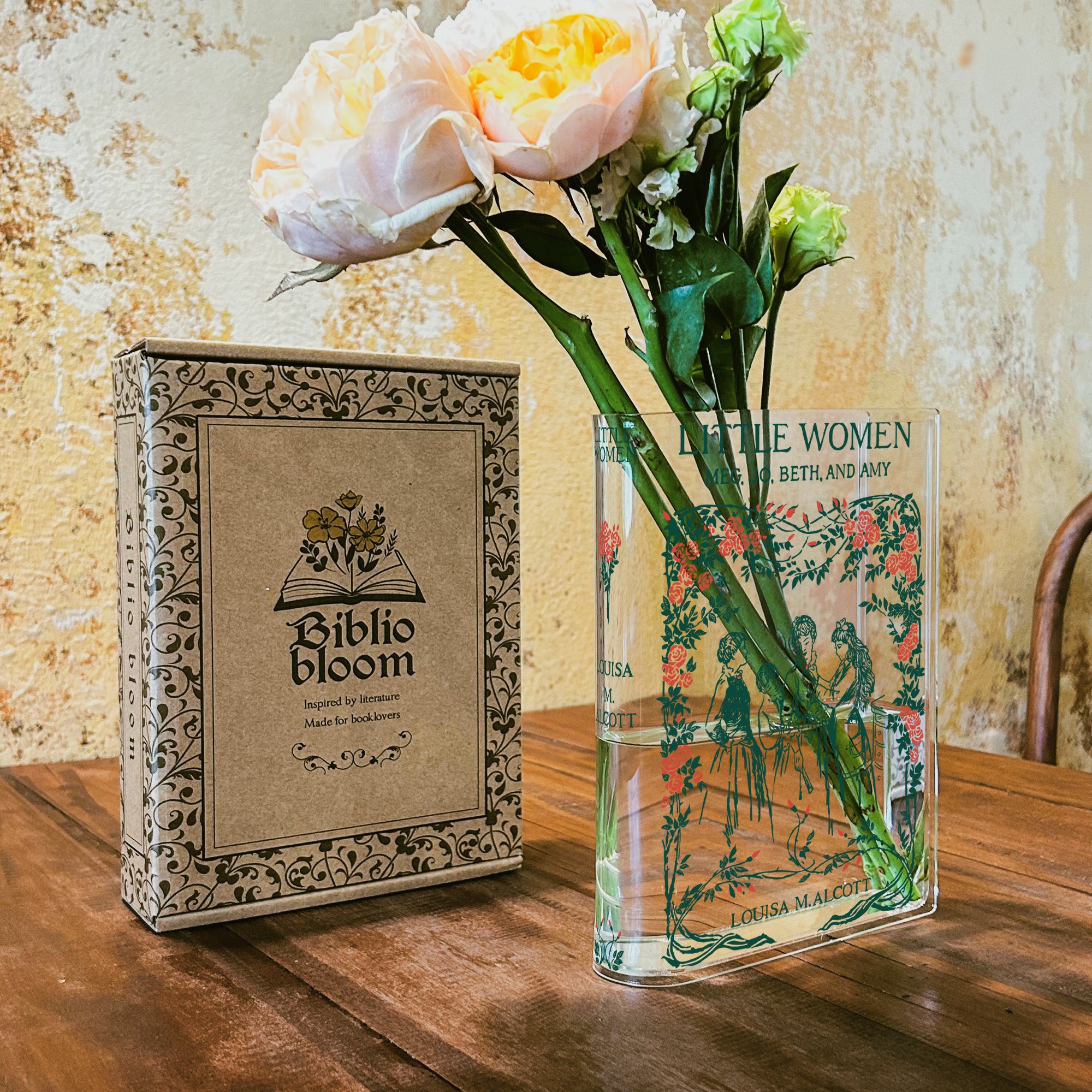 Acrylic Little Women book vase with flowers beside Biblio Bloom box on wooden table in cafe