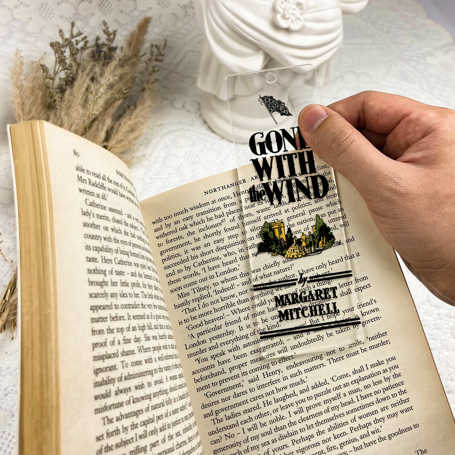 Hand holding clear Gone With the Wind bookmark on open book, vintage decor in background