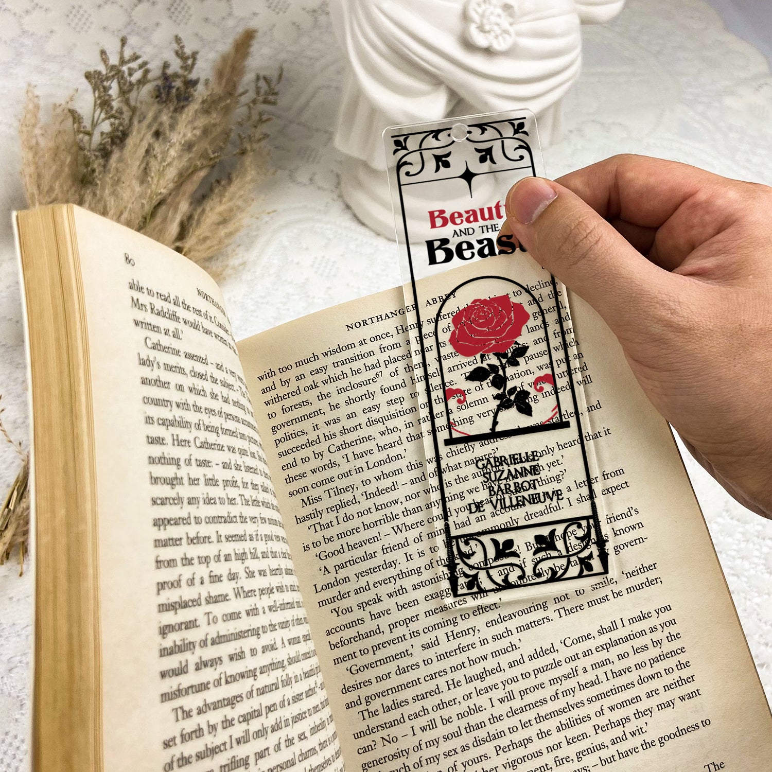 Hand holding Beauty and the Beast rose bookmark over open book on lace table