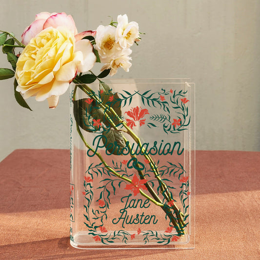 Acrylic book vase with Persuasion by Jane Austen, holding roses on a pink table.