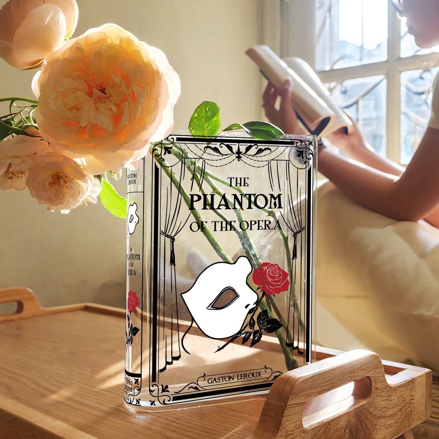 The Phantom of the Opera acrylic book vase with flowers on a wooden tray, person reading by window