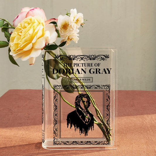 Acrylic book vase shaped like 'The Picture of Dorian Gray' with yellow roses on a table.