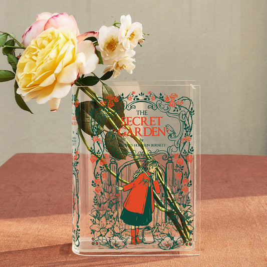 Acrylic book vase with The Secret Garden cover, fresh roses, on a pink tablecloth.