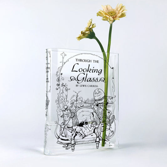 Through the Looking-Glass acrylic book vase with yellow gerbera flowers on white background.