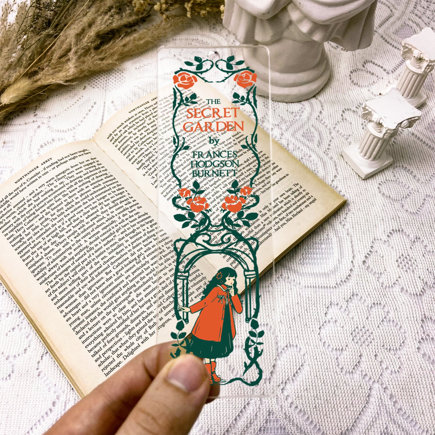 Hand holding transparent The Secret Garden bookmark over open vintage book on lace tablecloth