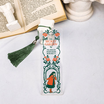 The Secret Garden bookmark with green tassel, beside open book and white column decor